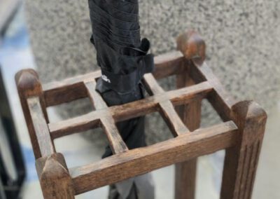 Umbrella in wooden stand near a chair.