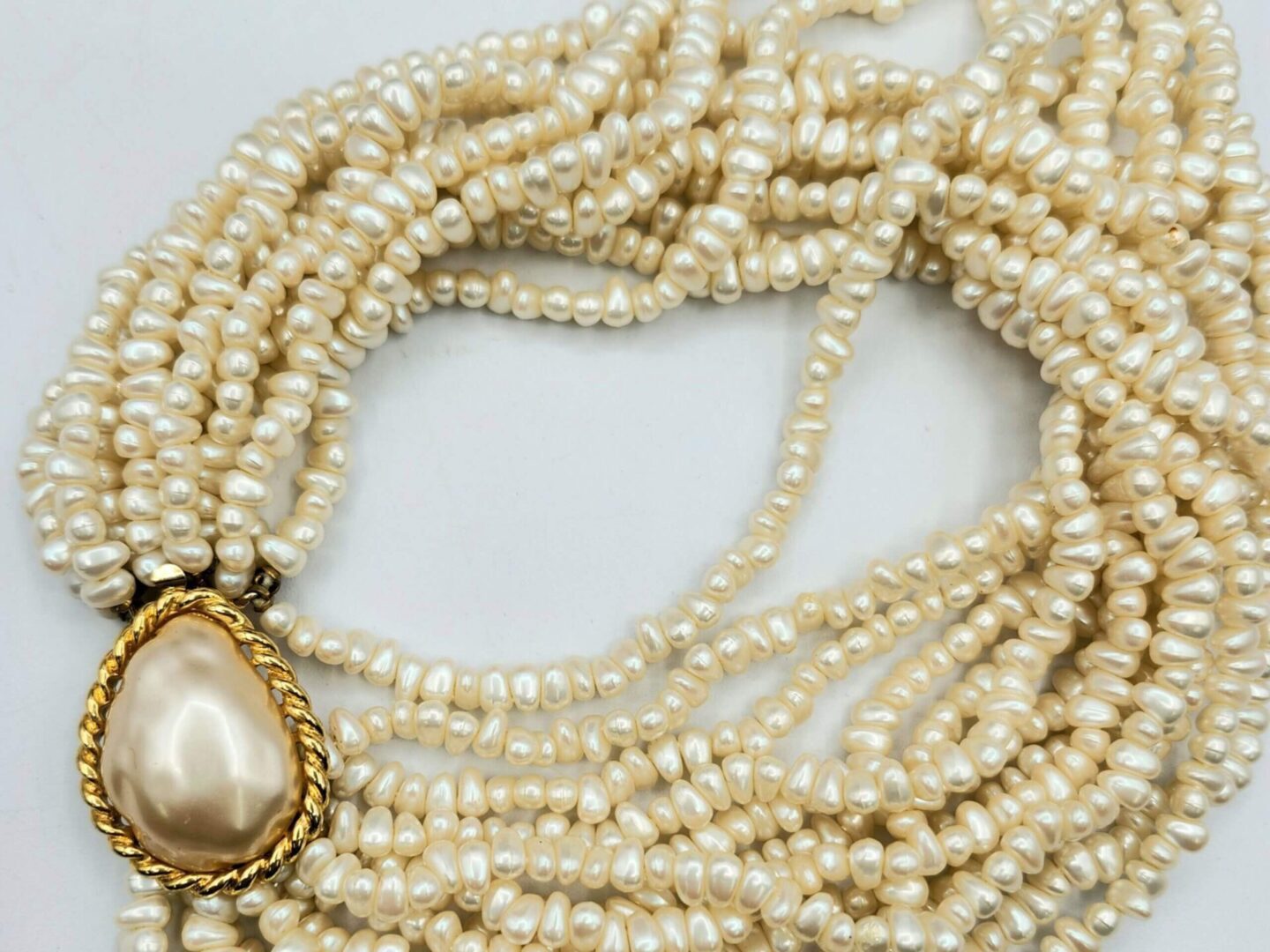 A multi-strand faux pearl choker necklace with a large teardrop clasp. 